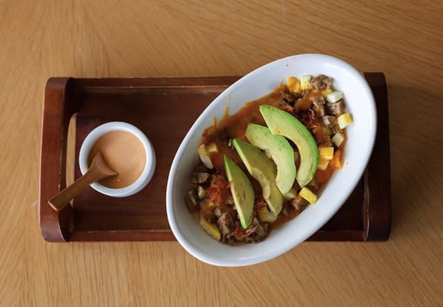 A bowl of avocado, egg, and sausage with a side of sauce