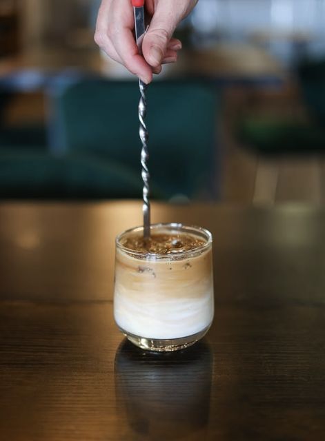 A layered iced latte being stirred with a bar spoon