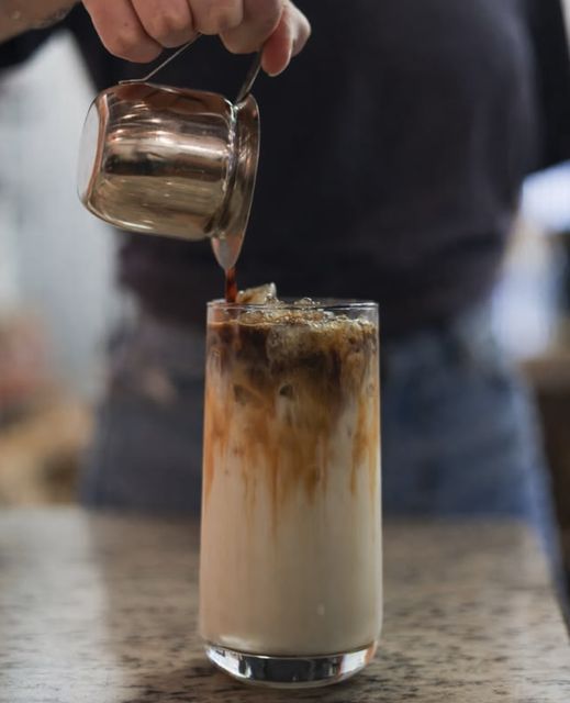 Espresso being poured over iced milk from a copper pitcher