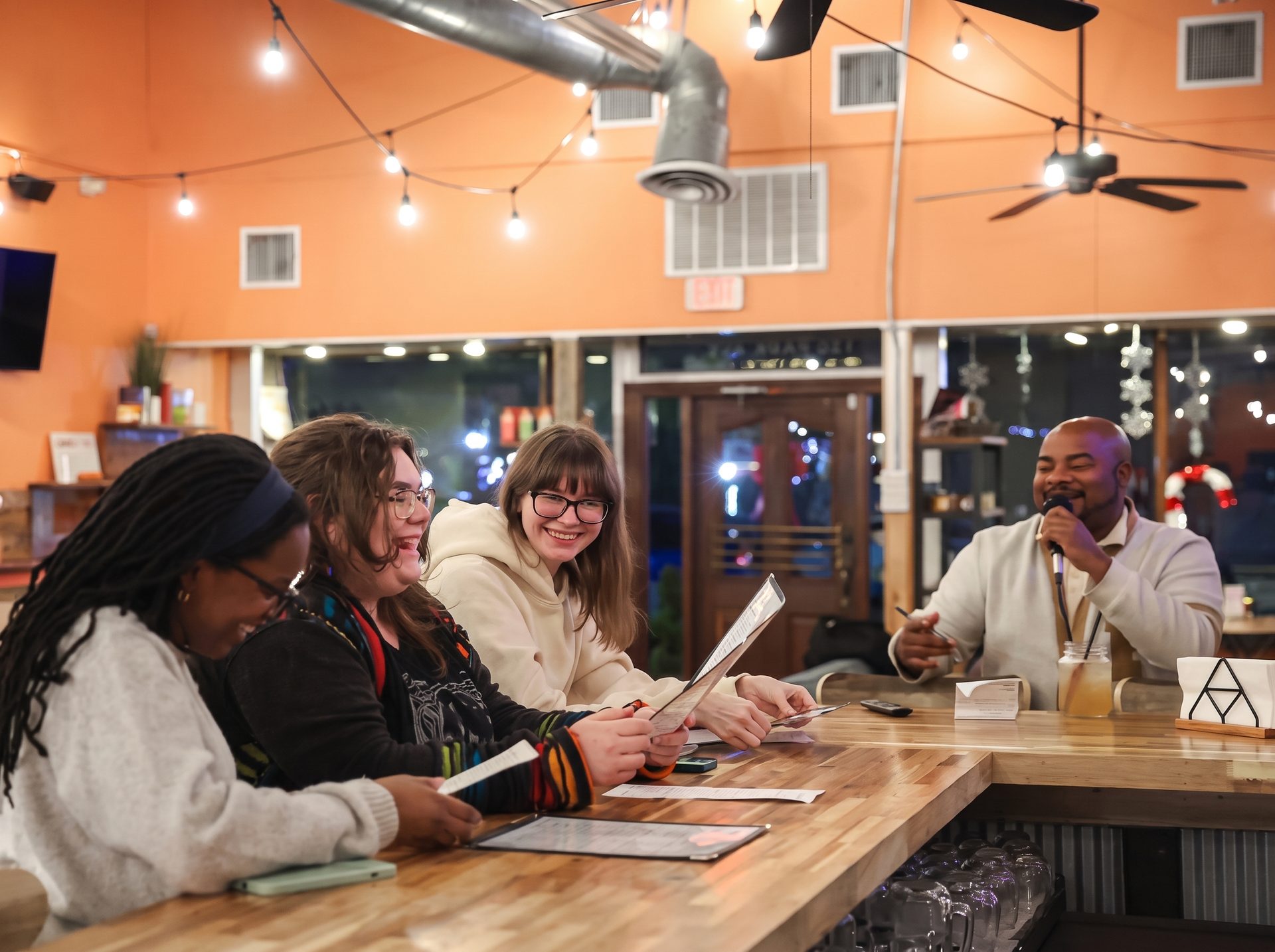 Friends laughing at the bar on karaoke night, with a host on the microphone